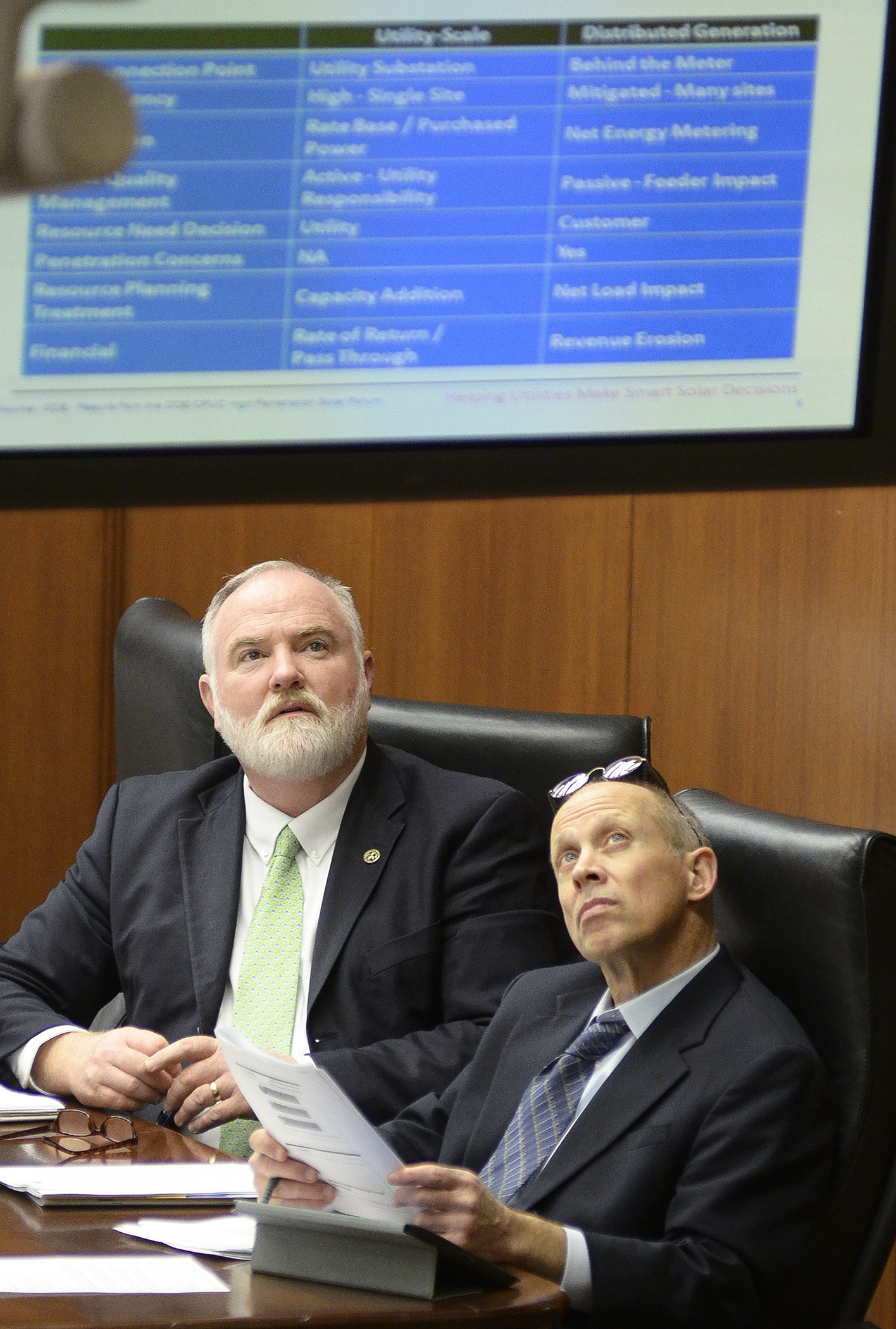 Rep. Bob Loonan, left, and Rep. Sheldon Johnson watch a presentation of net metering on a hearing room monitor during the Feb. 4 meeting of the House Job Growth and Energy Affordability Policy and Finance Committee.  Photo by Andrew VonBank